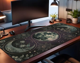 May include: A rectangular desk mat with a celestial design, featuring moons, flowers, and stars. The mat is black with green and gold accents, and sits beneath a computer monitor, mouse, and desk lamp. The desk is made of wood and the overall theme is a workspace.