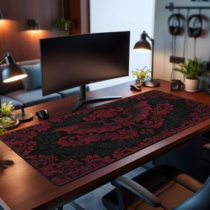 Puede incluir: Alfombrilla de escritorio negra y roja con un diseño gótico que presenta un murciélago con las alas extendidas y motivos florales. La alfombrilla es rectangular y cubre un escritorio de madera.