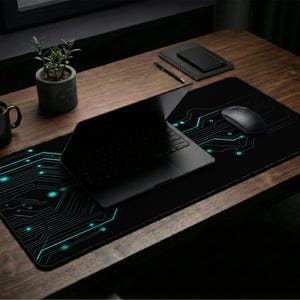 May include: A black mouse mat featuring a teal and black circuit board design. A black laptop, mouse, and coffee mug are on a wooden desk. A small potted plant is also visible.