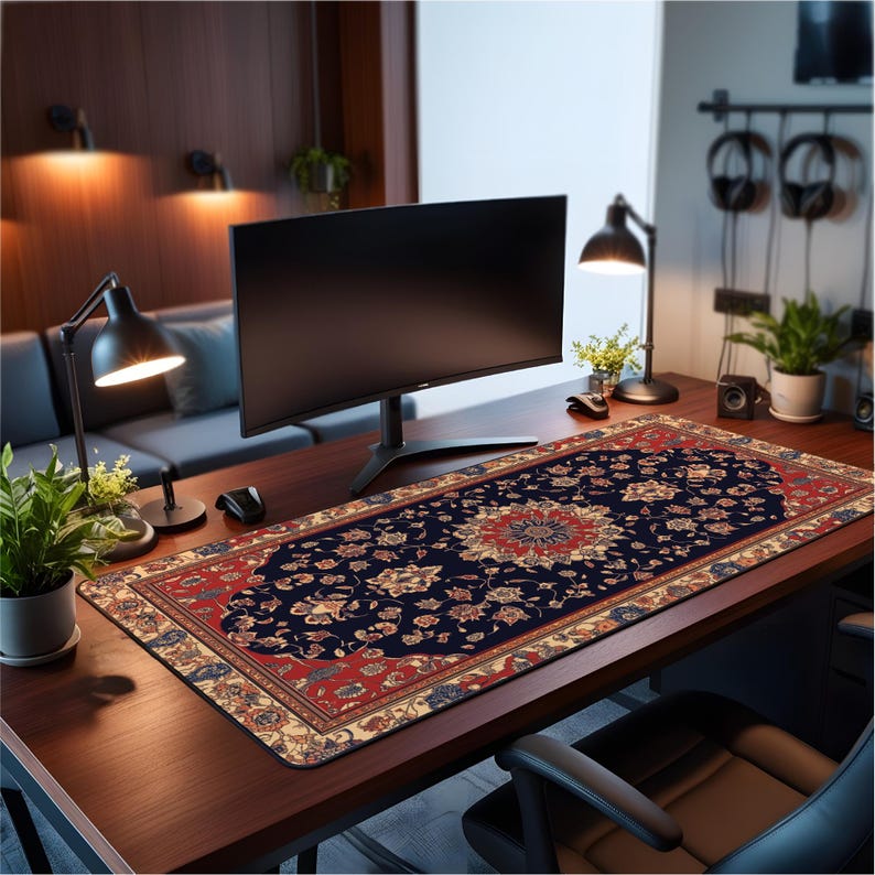 Desk mat with rich Persian rug print in navy, red, and gold floral pattern, styled on modern wood desk with curved monitor and plants
