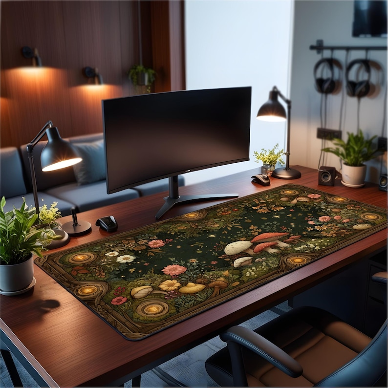 May include: A rectangular desk mat featuring a dark green background with a detailed illustration of various mushrooms, colorful wildflowers, and circular golden accents. The mat is positioned on a wooden desk surface in front of a computer monitor.