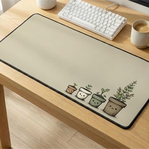 May include: A rectangular desk mat with a light beige surface and a black border. The bottom right corner features a line art illustration of four potted plants of varying sizes, each with a simple smiling face drawn on the pot.