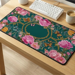 May include: A rectangular desk mat featuring a dark teal background with a pattern of large pink peony flowers, yellow and blue butterflies, and gold chain links. The mat has a black stitched border and a solid dark teal oval center area.