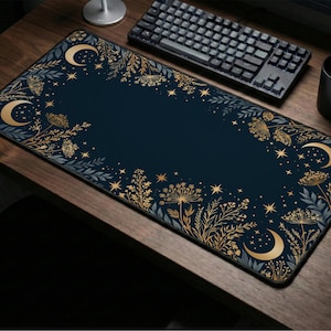 May include: A rectangular desk mat featuring a dark navy blue background with a decorative border of gold-colored crescent moons, stars, and botanical illustrations including wildflowers and leafy sprigs arranged along the edges.