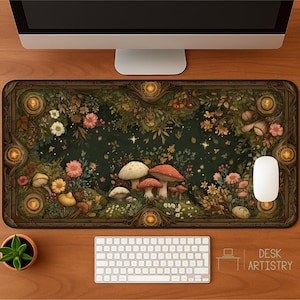 Puede incluir: Alfombrilla de escritorio rectangular con un diseño de bosque caprichoso con setas, flores y follaje en tonos verdes, marrones y rosas. La alfombrilla tiene un borde oscuro con elementos decorativos y el texto "DESK ARTISTRY". Se ven un ordenador, un teclado y un ratón.