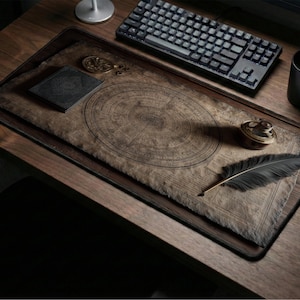 Könnte beinhalten: Ein Holztisch mit einem großen, rechteckigen Mauspads mit einem Vintage-Kartendesign. Eine schwarze Tastatur, Maus und ein Becher befinden sich auf dem Schreibtisch, zusammen mit einem kleinen Notizbuch, einer Taschenuhr und einer schwarzen Feder.