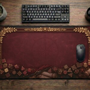 May include: A rectangular desk mat featuring a deep red surface with a central compass rose design, framed by a gold laurel leaf border. The bottom edge is decorated with various polyhedral dice and rolled parchment scrolls in shades of red and gold.