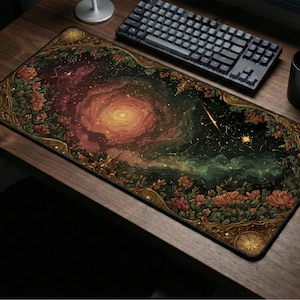 May include: A rectangular mouse pad featuring a vibrant cosmic design with a central galaxy and a shooting star. The border is adorned with floral and ornate patterns in shades of gold, red, and green. A black keyboard, mouse, and mug are on the wooden desk.
