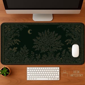 May include: A rectangular desk mat featuring a dark green background with gold-toned line art of a large tree, surrounding foliage, and a crescent moon. The mat has a decorative border and is positioned under a computer monitor and keyboard.