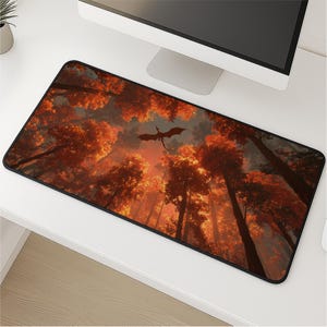 Puede incluir: Alfombrilla de ratón rectangular con una escena de fantasía de un dragón volando sobre un bosque de árboles altos con follaje naranja y rojo. La alfombrilla tiene un borde negro y está colocada sobre un escritorio blanco.