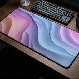 May include: A large rectangular mouse pad with a flowing, abstract design in shades of pink, purple, and blue. The mouse pad is on a wooden desk, next to a black keyboard, mouse, and mug.