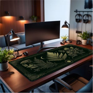 May include: A dark green rectangular desk mat with a gold botanical design featuring ferns, flowers, and a crescent moon. The mat is on a wooden desk with a computer monitor, desk lamp, and potted plants.
