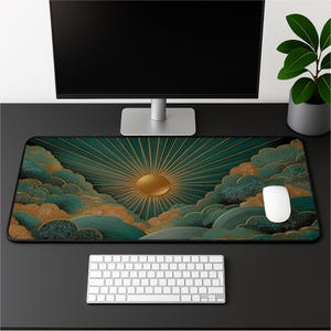 May include: A rectangular desk mat featuring a graphic print of a golden sun with radiating beams set against a background of stylized teal and gold clouds. The mat has a black border and is positioned on a desk with a white keyboard and mouse.
