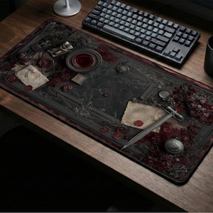 May include: A dark, rectangular desk mat with a gothic design featuring a sword, antique documents, and floral accents. The mat has a black border and a detailed, textured surface. A keyboard, mug, and mouse are also visible.