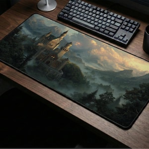 Puede incluir: Alfombrilla de ratón rectangular con una pintura detallada de un castillo en un bosque brumoso. Un teclado, una taza negra y un ratón están sobre un escritorio de madera. La paleta de colores incluye verdes, marrones y amarillos.