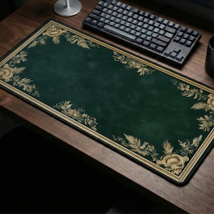 Puede incluir: Una alfombrilla de escritorio rectangular con una superficie de color verde bosque profundo y un borde decorativo en tono dorado. Las esquinas y los bordes están adornados con intrincadas ilustraciones botánicas de hojas y flores en oro.