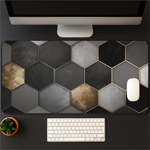 May include: A large rectangular mouse pad with a geometric pattern of gray, black, and gold hexagons. The pad has a gold border and is surrounded by a keyboard, mouse, and a small potted plant on a black surface.