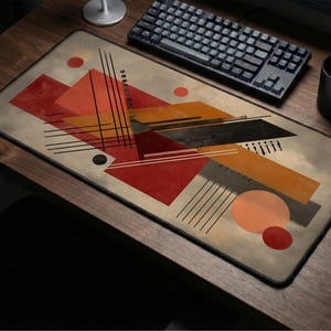 May include: Rectangular mouse pad with an abstract geometric design in shades of red, orange, black, and gray. The design features triangles, circles, and lines. A keyboard, mouse, and mug are visible.