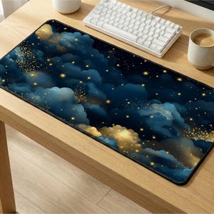 May include: A rectangular mouse pad featuring a dark blue and gold celestial design. The pad displays a night sky with fluffy clouds and sparkling stars. A white keyboard and coffee cup are visible on the wooden desk.