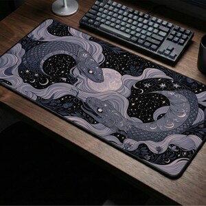 May include: A rectangular desk mat featuring a dark illustration of two serpents intertwined amidst swirling light purple clouds, stars, and a full moon. The design includes intricate scales, floral elements, and celestial patterns on a black background.