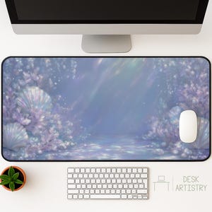 Puede incluir: Alfombrilla de escritorio rectangular con una escena submarina de ensueño con conchas marinas y coral en tonos morados y azules. Un ratón y un teclado blancos están sobre la alfombrilla. Las palabras "DESK ARTISTRY" están en la esquina inferior derecha.