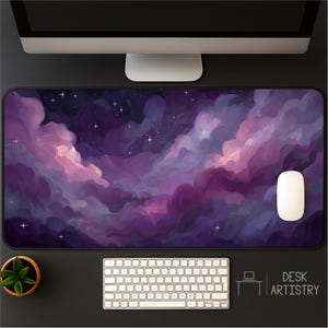 Op de afbeelding: Een grote rechthoekige bureaumat met een levendige, artistieke weergave van een paarse en roze nevel met verspreide sterren. Een witte computermuis, toetsenbord en monitor zijn zichtbaar. De mat heeft de tekst "DESK ARTISTRY".