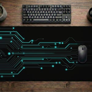 May include: A black rectangular mouse pad with a teal circuit board design. A black computer mouse rests on the pad. A black keyboard, a cup of coffee, and a small potted plant are also visible on a wooden surface.