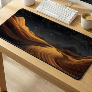 May include: A rectangular desk mouse pad featuring a golden, textured landscape design under a starry night sky. The pad has a black border and is placed on a wooden desk, alongside a white keyboard and a cup of coffee.