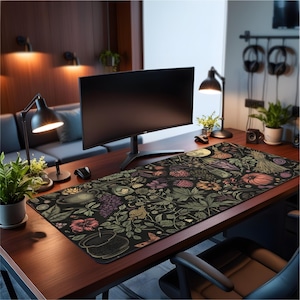 May include: A large, rectangular desk mat with a dark background and a botanical design featuring various plants, fruits, and a full moon. The mat is placed on a wooden desk, with a computer monitor and other office accessories.