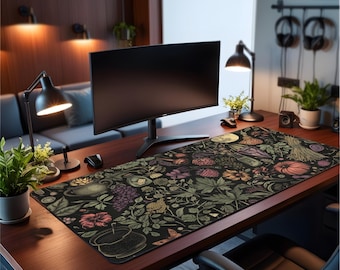 May include: A rectangular desk mat with a dark background and a botanical design featuring plants, fruits, and a full moon. The mat is on a wooden desk, with a computer monitor and other office accessories. The mat's length is approximately 80 cm.