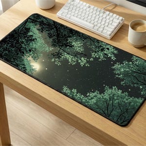 Puede incluir: Alfombrilla de ratón rectangular con un diseño de bosque nocturno. El diseño presenta árboles y follaje verde oscuro que enmarcan un cielo estrellado con una luna brillante. La alfombrilla está sobre un escritorio de madera con un teclado y una taza de café.