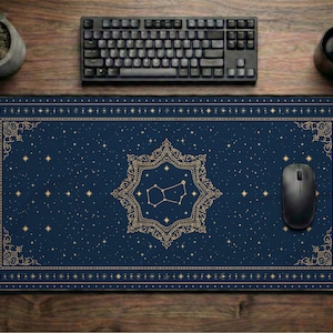 May include: A rectangular desk mat featuring a dark blue background with gold celestial patterns, including a central star constellation framed by an ornate border, stars, and dots. The mat is positioned under a black computer keyboard and mouse.