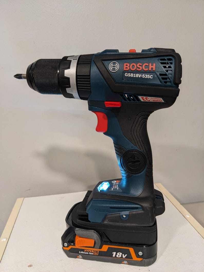 Puede incluir: Un taladro inal&aacute;mbrico azul y negro con una bater&iacute;a negra y naranja. El taladro tiene el logotipo de Bosch y el n&uacute;mero de modelo GSB18V-535C. La bater&iacute;a tiene el texto "HYPER LI Lithium Ion 18V".