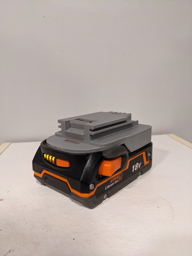 Pu&ograve; includere: Una batteria Hyper Tough agli ioni di litio da 18 V di colore grigio e nero con un pulsante arancione e un indicatore del livello della batteria.