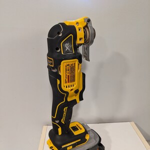 May include: A yellow and black cordless oscillating tool with a brushless motor. The tool is attached to a black and orange battery pack with the word "RIDGID" printed on it.
