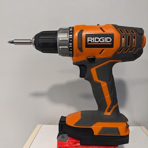 May include: An orange and black cordless drill with a black and red battery pack. The drill has a black handle and a silver chuck. The battery pack is labeled "CRAFTSMAN V20 2.0 Ah LITHIUM ION".