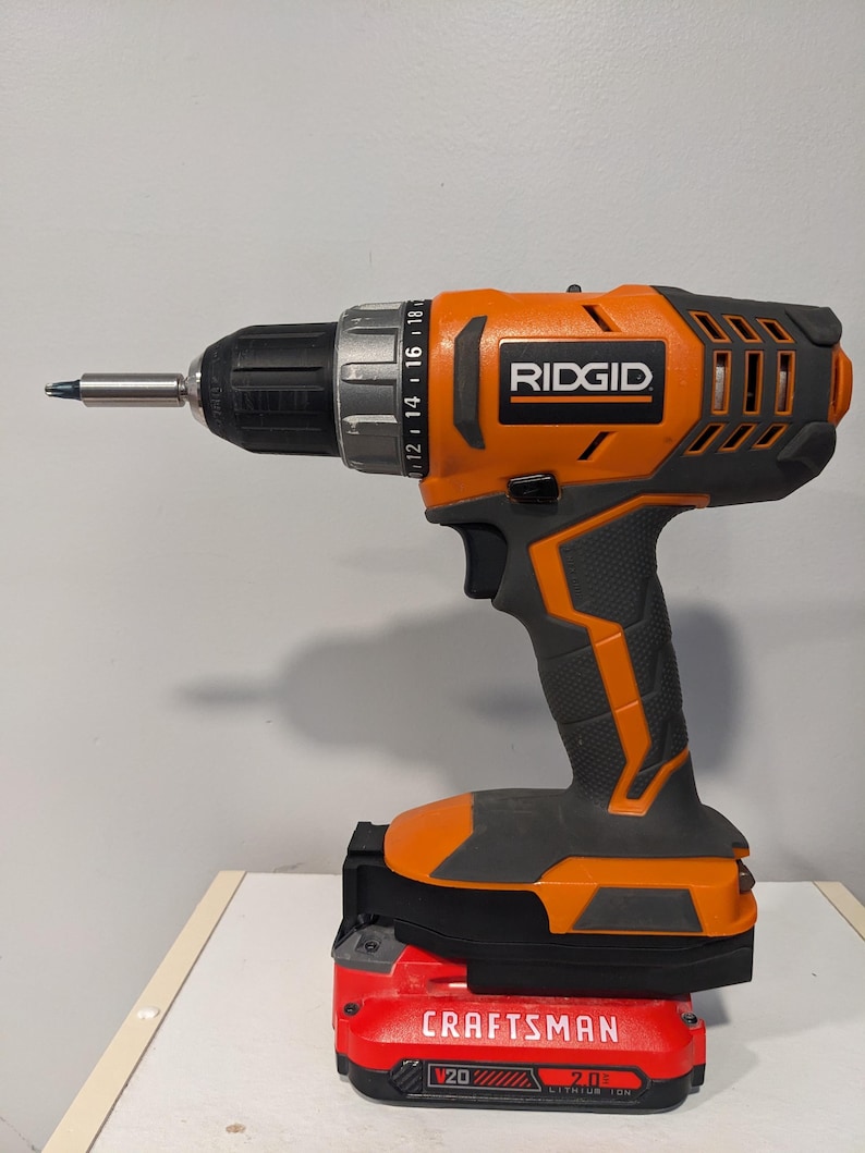 May include: An orange and black cordless drill with a black and red battery pack. The drill has a black handle and a silver chuck. The battery pack is labeled "CRAFTSMAN V20 2.0 Ah LITHIUM ION".
