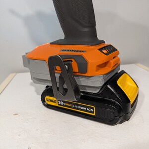 May include: A black and orange cordless drill with a 20V MAX lithium-ion battery. The drill has a black handle and a silver belt clip. The battery is labeled "DEWALT 20V MAX LITHIUM ION".