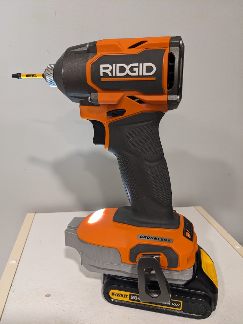 May include: An orange and black cordless drill with a black battery pack. The drill has a black handle and a silver trigger. The battery pack is labeled "DEWALT 20V MAX* LITHIUM ION". The drill is labeled "RIDGID" and "BRUSHLESS".