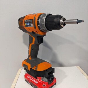 May include: An orange and black cordless drill with a red battery pack that says "CRAFTSMAN" on it. The drill has a black chuck and a silver gear selector.