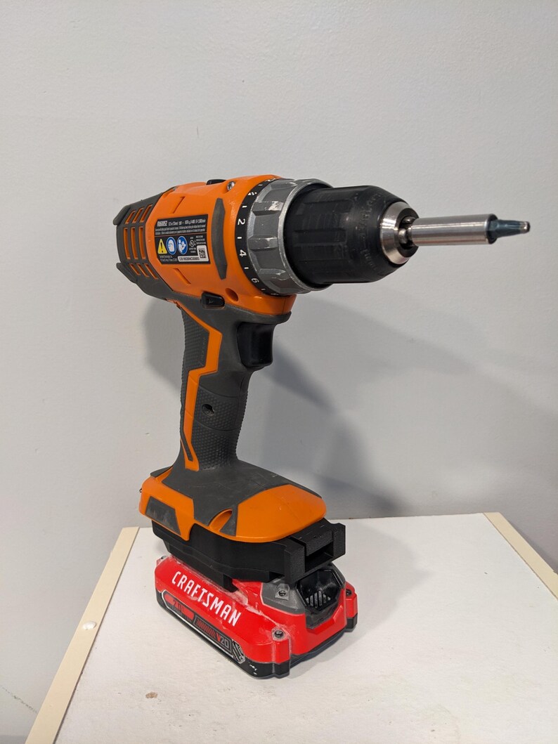 May include: An orange and black cordless drill with a red battery pack that says "CRAFTSMAN" on it. The drill has a black chuck and a silver gear selector.