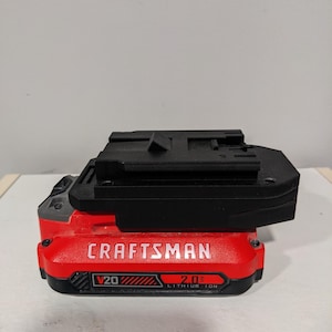 Pode incluir: Uma bateria vermelha e preta Craftsman V20 2.0 Ah de íons de lítio com um adaptador de plástico preto no topo.