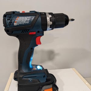 Puede incluir: Un taladro inal&aacute;mbrico azul y negro con un portabrocas negro y un dial de ajuste de torque plateado. El taladro est&aacute; conectado a una bater&iacute;a naranja y negra que dice "RIDGID HYPER LI Lithium Ion".