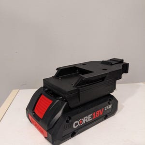 Op de afbeelding: Een zwarte en rode Bosch CORE18V 4.0 Ah accu met een zwarte kunststof montagebeugel.