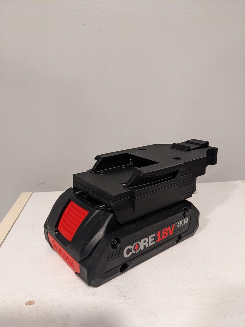 Op de afbeelding: Een zwarte en rode Bosch CORE18V 4.0 Ah accu met een zwarte kunststof montagebeugel.