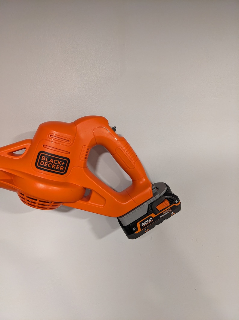 Pu&ograve; includere: Un soffiatore per foglie senza fili arancione e nero con una batteria nera etichettata "RIGID 18V Lithium Ion". Il soffiatore per foglie &egrave; prodotto da BLACK+DECKER.