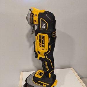 May include: A yellow and black DeWalt 20V MAX XR cordless oscillating tool with a brushless motor and a 18V battery. The tool is on a white surface.