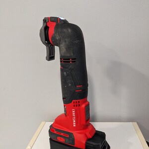 May include: A red and black Craftsman cordless oscillating tool with a black and orange Ridgid battery pack. The tool has a built-in LED light and a flexible shaft.