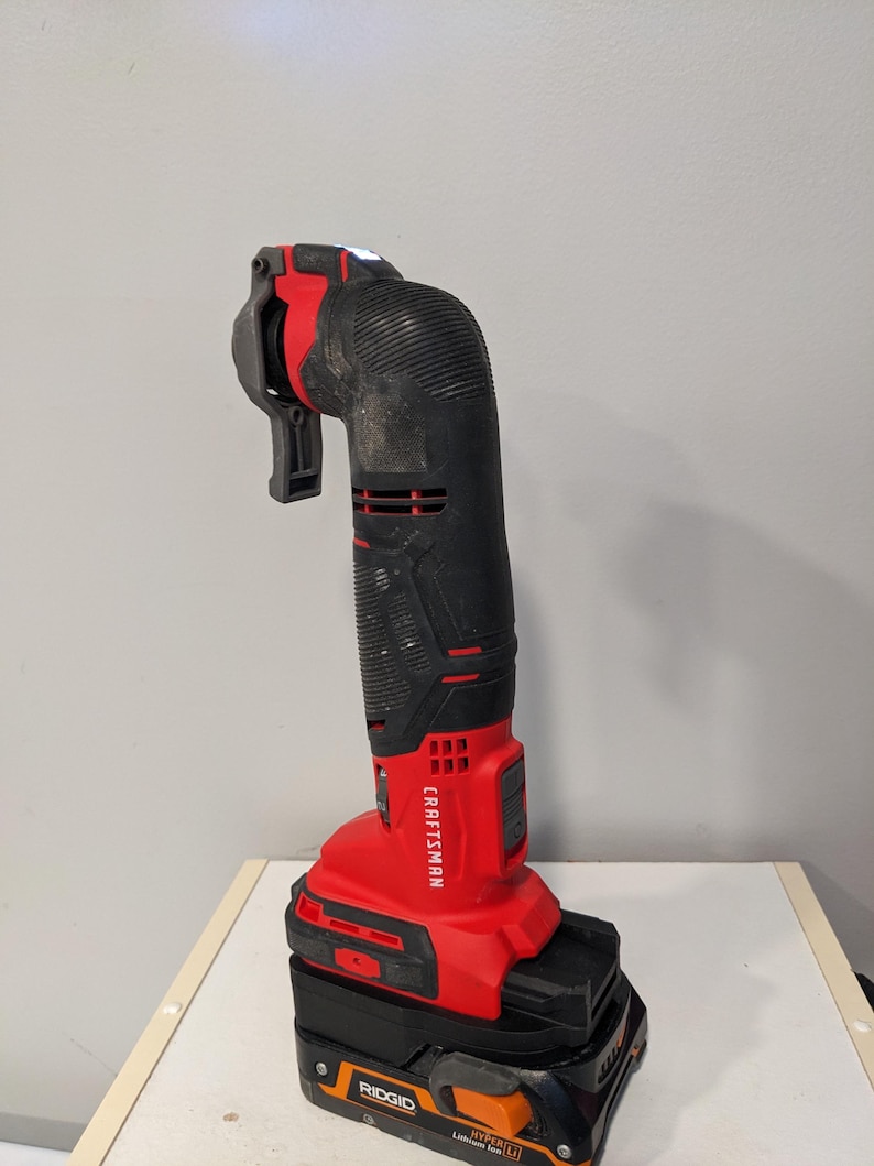 May include: A red and black Craftsman cordless oscillating tool with a black and orange Ridgid battery pack. The tool has a built-in LED light and a flexible shaft.