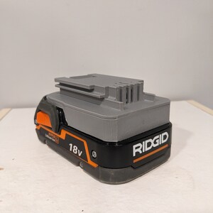 Pu&ograve; includere: Una batteria Ridgid da 18 V di colore grigio e nero con un pulsante arancione e il testo "HYPER LI Lithium Ion" e "RIDGID" sul lato.